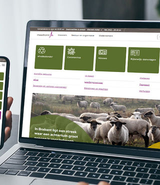 Foto van een hand die een mobiele telefoon vast houdt en een laptop, met op beide schermen de website van gemeente Maashorst