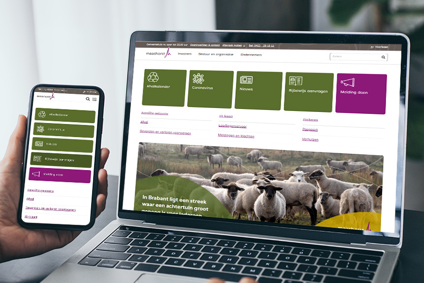 Foto van een hand die een mobiele telefoon vast houdt en een laptop, met op beide schermen de website van gemeente Maashorst