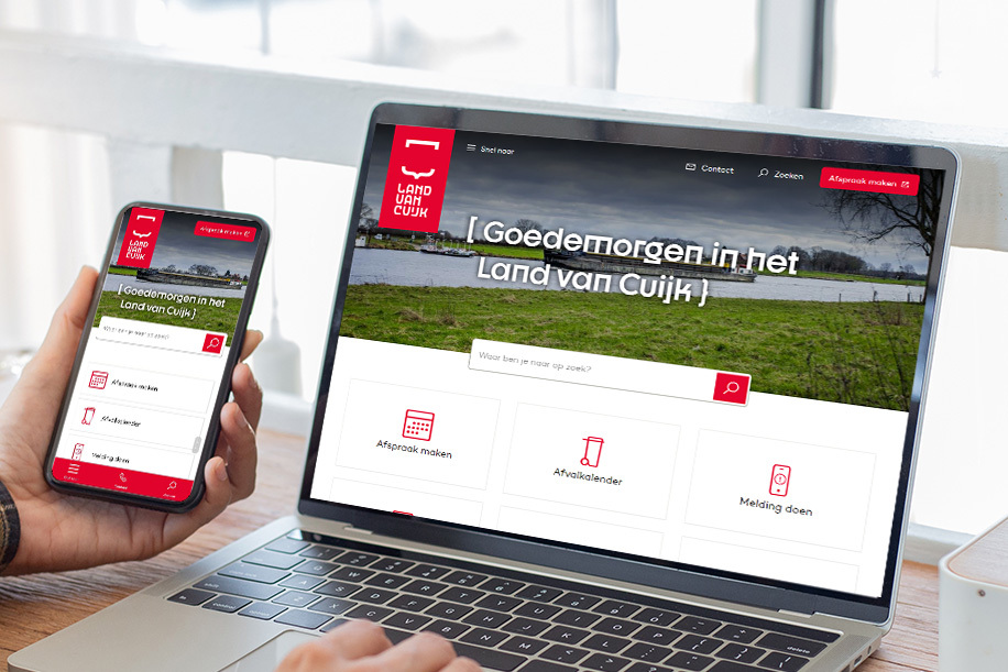Foto van een hand die een mobiele telefoon vasthoud en een laptop, op beide schermen zie je de homepage van de website van gemeente Land van Cuijk